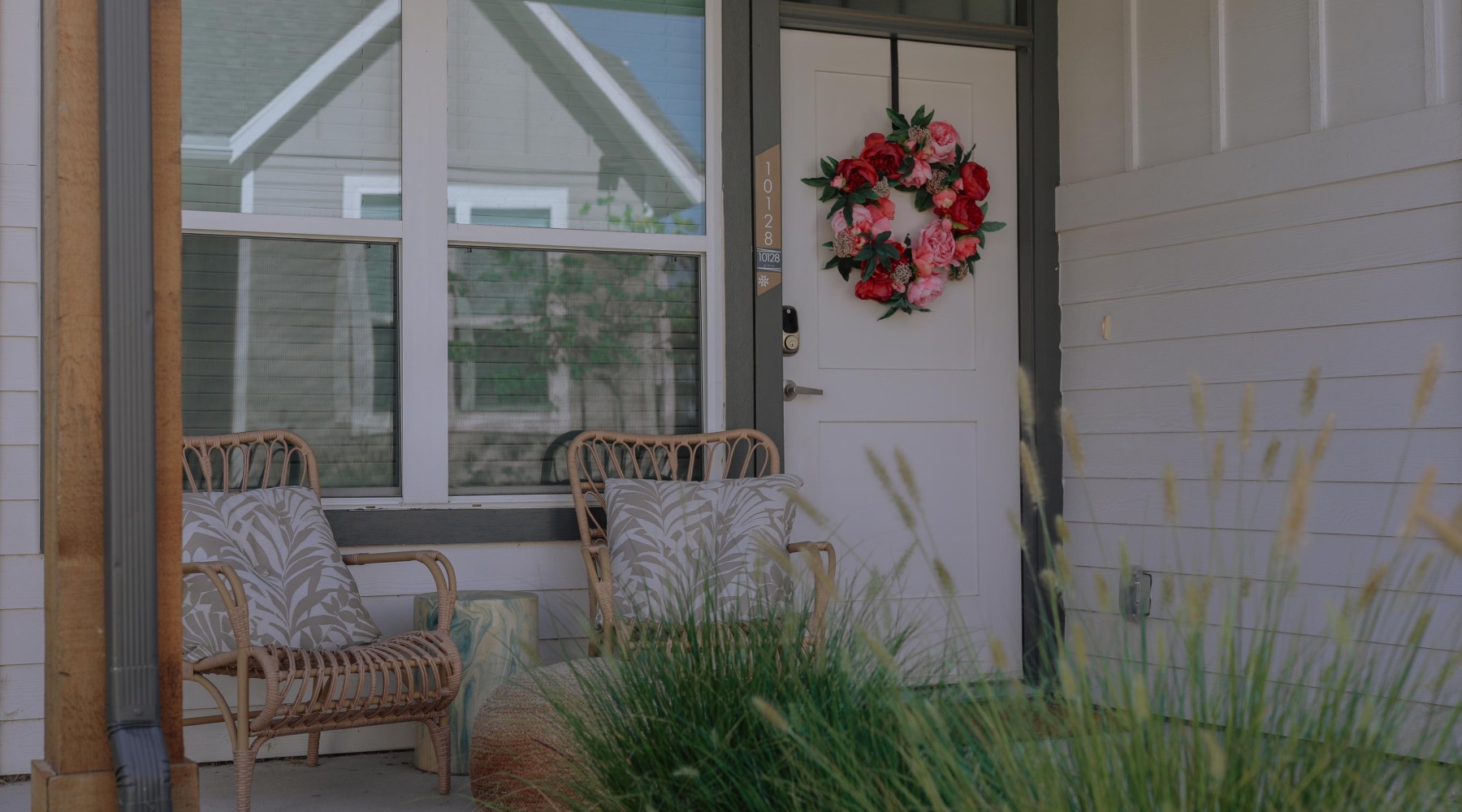 Charming front porch of a modern Fort Worth apartment home featuring private entry, stylish rattan patio seating, and a bold floral wreath on the front door. Thoughtfully designed outdoor space includes tall decorative grasses and cozy seating, highlighti Charming front porch of a modern Fort Worth apartment home featuring private entry, stylish rattan patio seating, and a bold floral wreath on the front door. Thoughtfully designed outdoor space includes tall decorative grasses and cozy seating, highlighti