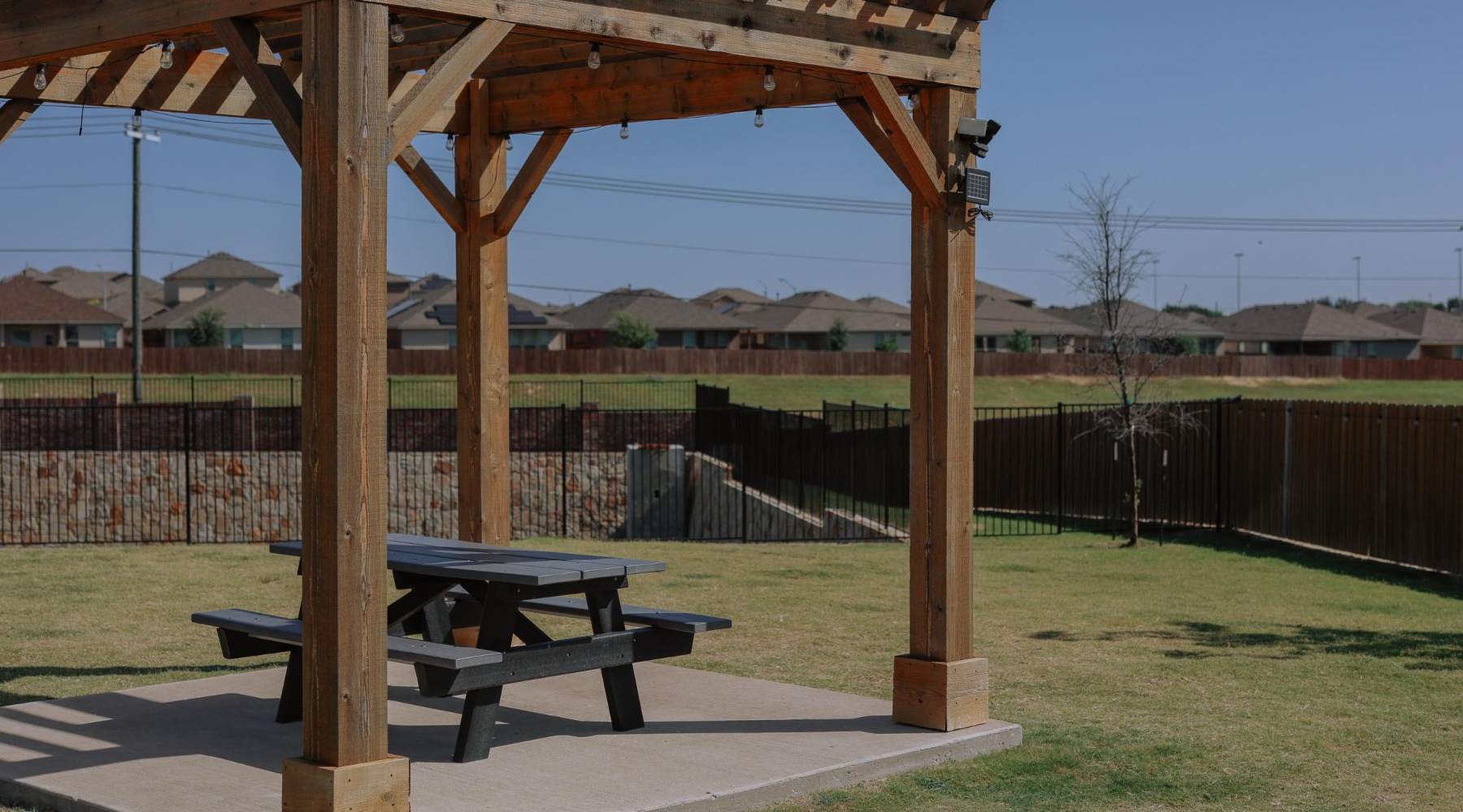 Dog Park & Dog Friendly Spacious dog park at Chapel Creek Cottages in Fort Worth, TX, featuring a shaded pergola with picnic seating and wide open grassy areas perfect for pets to play and socialize. This pet-friendly rental community offers private yards, luxury amenities, and